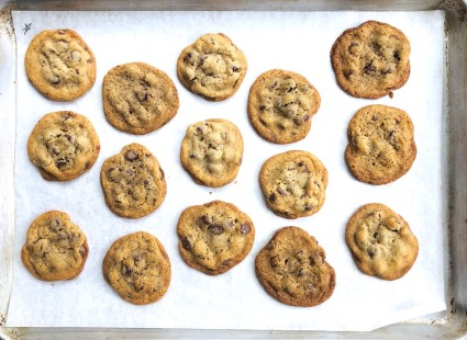 Baked chocolate chip cookies in staggered rows on a baking sheet.