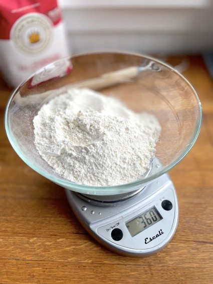 Bowl of flour on a digital scale; bag of flour in the background.