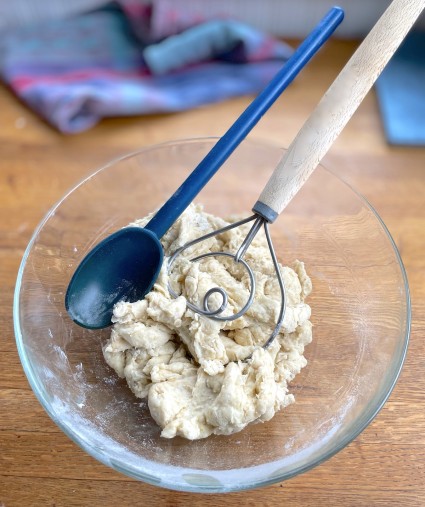 Blue stirring spoon and Danish dough whisk in a bowl of yeast dough.