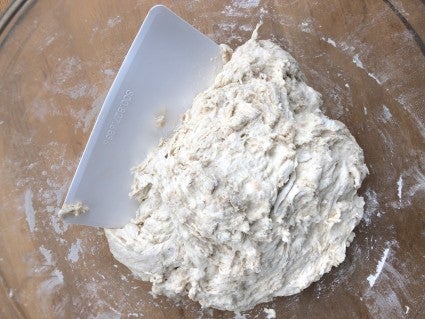 Plastic bowl scraper in a  clear glass bowl of sticky yeast dough.