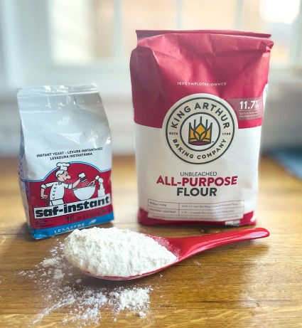 Bags of SAF Red instant yeast and King Arthur Unbleached All-Purpose Flour on a wooden countertop.