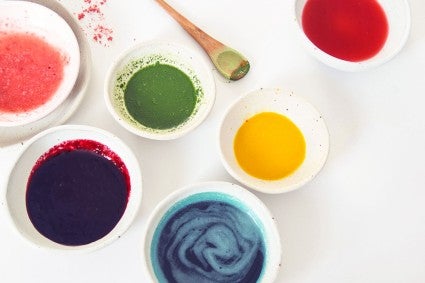 Variety of natural food colorings in bowls, including pink, blue, yellow, and green