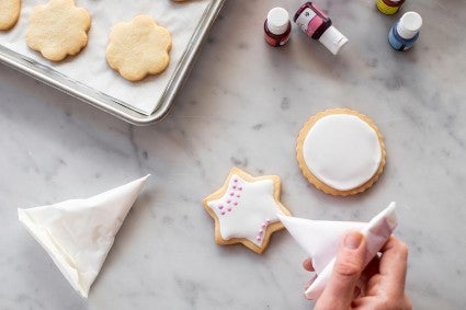 Cornet being used to add pink dots to the surface of an iced cookie