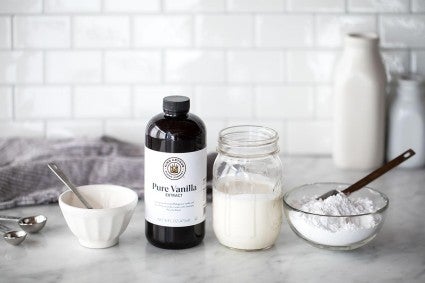 A mason jar filled with heavy cream next to a bottle of vanilla extract and confectioners' sugar