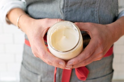 A baker holding an open jar of whipped cream, showing the soft texture
