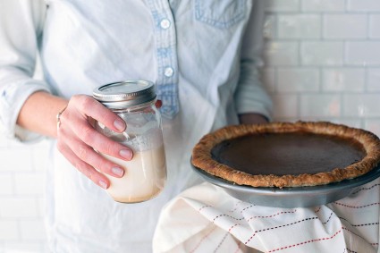 A baker holding a pumpkin pie and jar of mason jar whipped cream, as if getting ready to leave