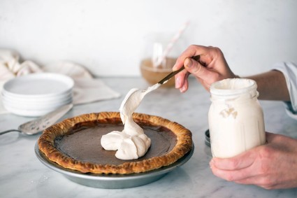 A baker's hand dolloping cream on top of a pumpkin pie