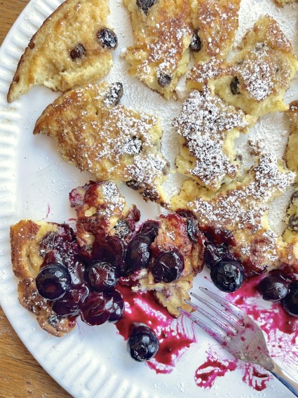 Kaiserschmarrn torn into pieces on a serving plate, blueberry compote ladled on top.