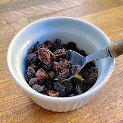 Raisins soaked in rum in a small white bowl.