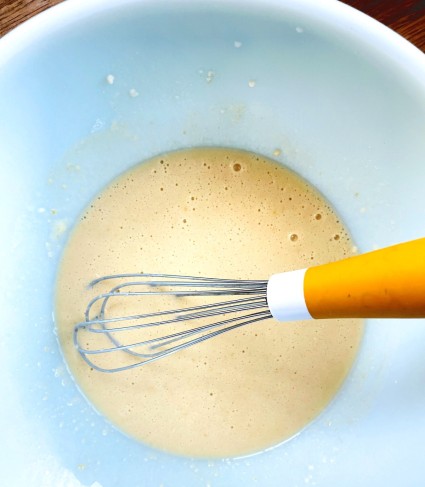 Pancake mix stirred together with liquid ingredients in a blue Pyrex bowl.