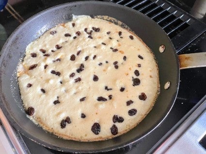 Kaiserschmarrn being cooked in a 10" frying pan, rum-soaked raisins sprinkled on top.