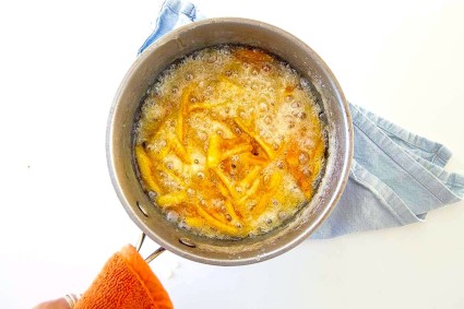 Orange peel simmering in simple syrup in a saucepan.