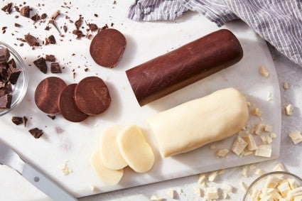 Logs of dark and white modeling chocolate on a cutting board, partially sliced