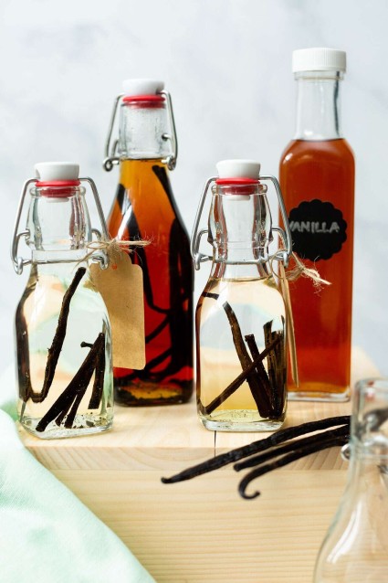 Decorative bottles of homemade vanilla extract, some with vanilla beans inside, plus vanilla bans on the counter beside them.