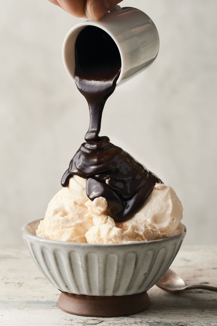 Hot fudge sauce being poured over a dish of vanilla ice cream.