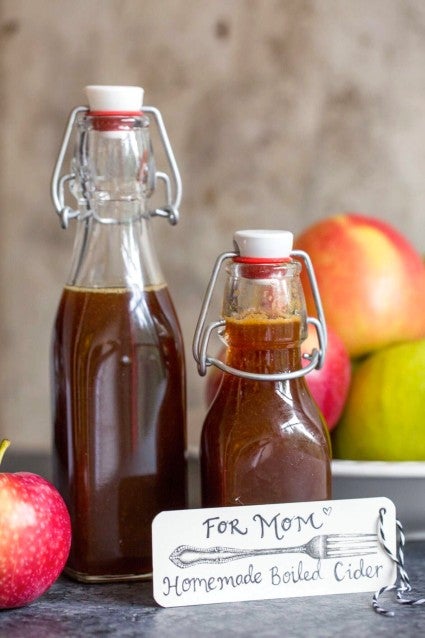 Homemade boiled cider in a couple of decorative gifts jars, whole apples in the background.