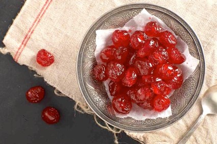 Homemade candied cherries in a clear glass bowl sitting atop a cream-colored dish towel.