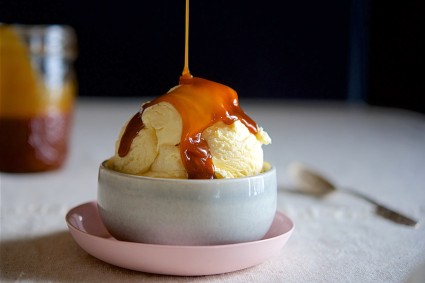 Caramel sauce being drizzled over a bowl of vanilla ice cream.