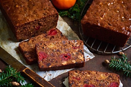 Dark fruitcake slices on a plate, two loaves in the background.