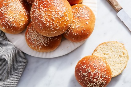 Beautiful Burger Buns piled on a plate on a white table, one cut open.