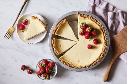 Easy Cheesecake in its round pie pan, one slice on a plate beside the pan, garnished with fresh strawberries/