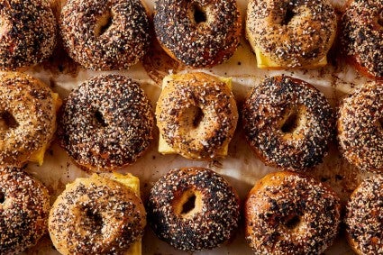 A dozen everything-topped bagels, some made into egg sandwiches, on a table.