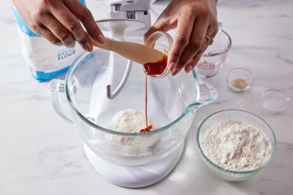A baker adding barley malt syrup to bagel dough