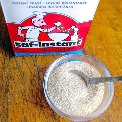 Bowl of SAF Red yeast with measuring spoon, package of  yeast in the background.