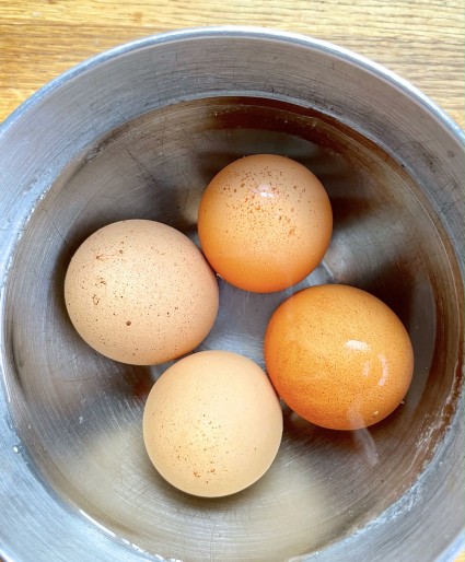 Four brown eggs in a stainless steel bowl, covered with hot water.