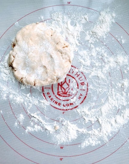 Flattened disk of pie pastry on a floured silicone rolling mat.