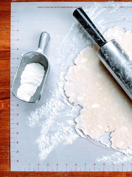 Rolled out pie pastry on a floured rolling mat, with rolling pin and flour scoop.