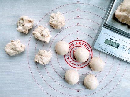Portions of yeast dough on a rolling mat, some roughly portioned, some shaped into smooth, round balls.