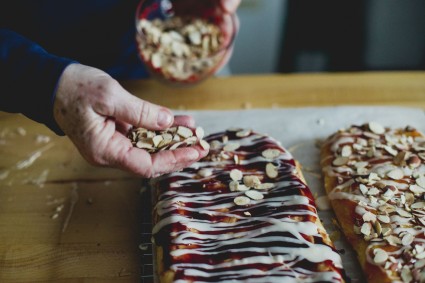Elder woman's hand sprinkling almonds onto pastry
