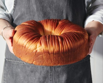 Baker holding baked loaf of wool roll bread