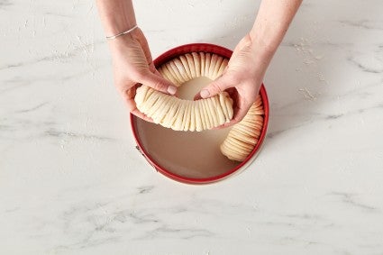 Baker placing pieces of wool roll bread into a springform pan