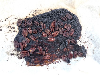 Burned pecans in a black puddle of burned sugar.