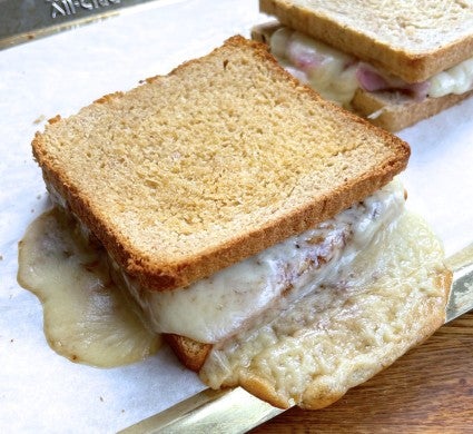 Grille cheese sandwich on a parchment-lined pan, cheese oozing like a lava flow out of the sandwich.