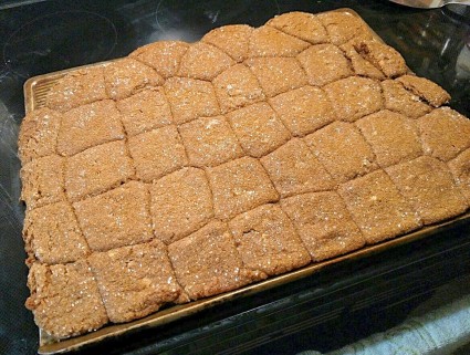 Ginger cookies on a baking sheet in the oven all puffed and melted together into what looks like a big gingerbread brownie.