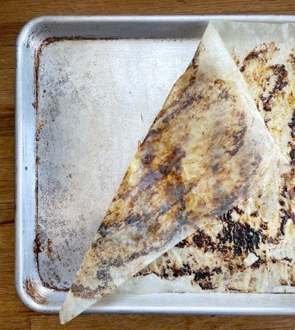 Baking heet lined with grease-stained parchment, parchment pulled back to show the clean pan underneath.