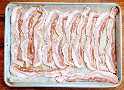 Raw bacon strips laid side by side on a parchment-lined baking sheet.