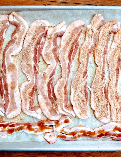 Raw bacon strips laid side by side on a parchment-lined baking sheet, and sprinkled with brown sugar.