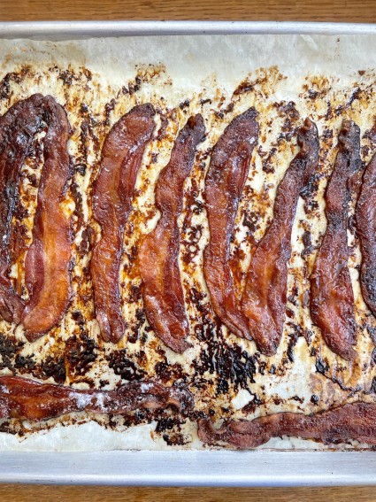 Baked candied bacon on a parchment-lined baking sheet.