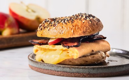 Breakfast sandwich on a bagel made with egg, cheese, apple, and candied bacon.