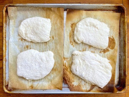 Four loaves of sourdough Pan de Cristal on parchment on a baking sheet, ready to rise