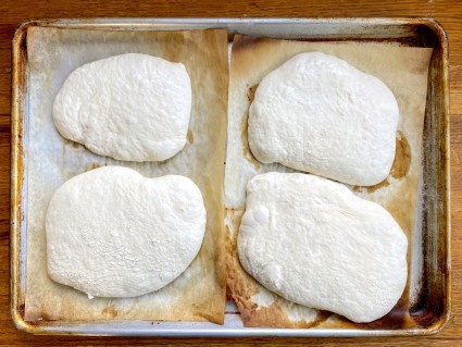 Four loaves of sourdough Pan de Cristal on parchment on a baking sheet, fully risen