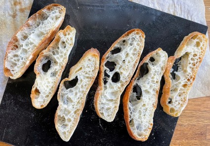 Slices of sourdough Pan de Cristal on black marble, cut crosswise to show their holey interior