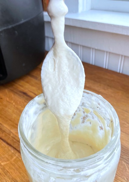 Spoon dripping sourdough starter into a bowl  to show the starter's thickness