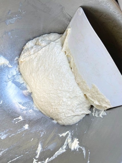 Very slack dough with a bowl scraper in the bottom of a mixing bowl