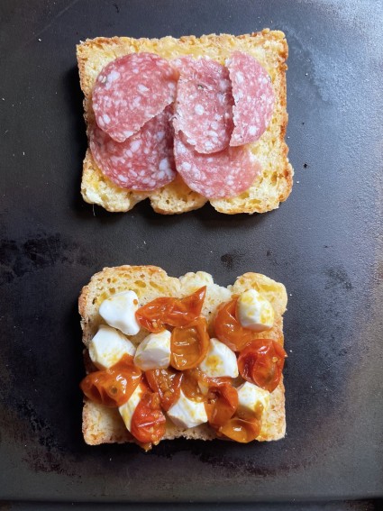 Roasted tomatoes, mini mozzarella balls, and sliced salami laid out on sliced of cheddar bread, ready to be griddled.