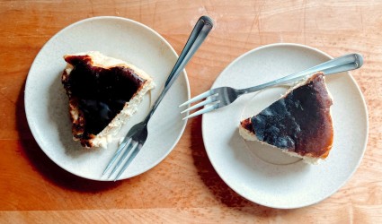 Two slices of Basque-style cheesecake on plates, with forks, on a wooden counter.